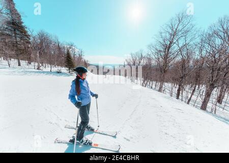 Femme skieuse faisant une pause pendant le ski en pente. Bonne femme active asiatique se détendant par beau temps à la station de ski. Vacances de sport d'hiver Banque D'Images