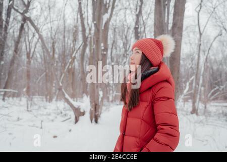 Femme asiatique heureuse à l'extérieur en hiver forêt de nature. Portrait d'une jeune femme ethnique multiraciale portant un chapeau et un manteau rouges Banque D'Images