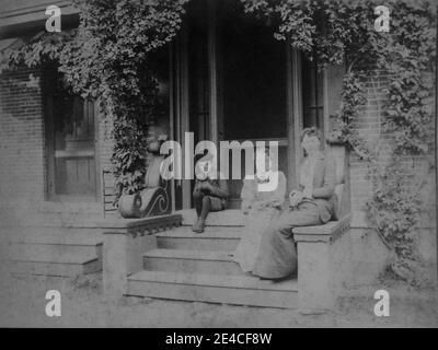 Archive américaine portrait monochrome de deux jeunes femmes et d'un enfant plus jeune assis sur des marches de porche devant une maison en briques. Prise à la fin du XIXe siècle à Port Byron, NY, États-Unis Banque D'Images