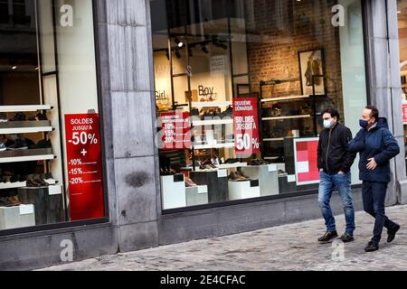 Bruxelles, Belgique. 22 janvier 2021. Des personnes portant des masques de visage marchent devant une boutique avec des affiches de vente à Bruxelles, Belgique, le 22 janvier 2021. Les ventes annuelles d'hiver en Belgique ont débuté le 4 janvier. Pour stimuler la consommation, les ventes d'hiver de quatre semaines prévues ont été prolongées de deux semaines jusqu'au 15 février. Credit: Zhang Cheng/Xinhua/Alay Live News Banque D'Images