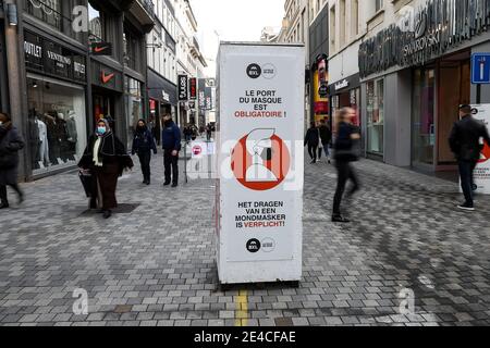 Bruxelles, Belgique. 22 janvier 2021. Les gens marchent devant un panneau rappelant aux gens de porter des masques sur une rue commerçante à Bruxelles, Belgique, le 22 janvier 2021. Les ventes annuelles d'hiver en Belgique ont débuté le 4 janvier. Pour stimuler la consommation, les ventes d'hiver de quatre semaines prévues ont été prolongées de deux semaines jusqu'au 15 février. Credit: Zhang Cheng/Xinhua/Alay Live News Banque D'Images