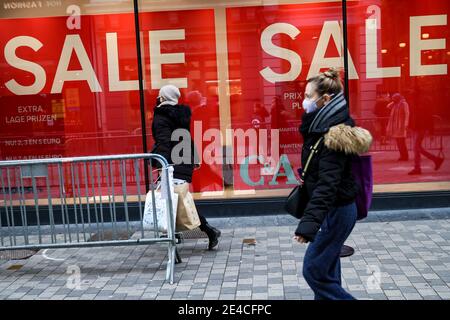 Bruxelles, Belgique. 22 janvier 2021. Des personnes portant des masques de visage marchent devant une boutique avec des affiches de vente à Bruxelles, Belgique, le 22 janvier 2021. Les ventes annuelles d'hiver en Belgique ont débuté le 4 janvier. Pour stimuler la consommation, les ventes d'hiver de quatre semaines prévues ont été prolongées de deux semaines jusqu'au 15 février. Credit: Zhang Cheng/Xinhua/Alay Live News Banque D'Images