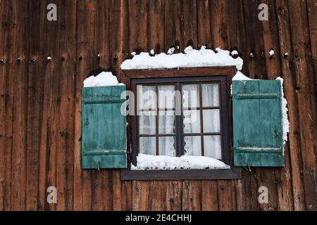 Une fenêtre avec des volets verts sur une ancienne ferme dans hiver avec neige Banque D'Images