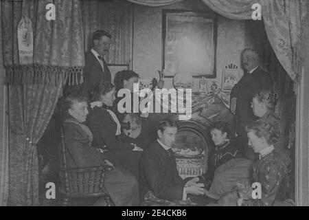 American archive monochrome portraitof un groupe de personnes à la maison appréciant le divertissement. Une femme joue un banjo. Prise à la fin du XIXe siècle à Byron, NY, États-Unis Banque D'Images