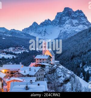 Italie, Vénétie, Belluno, Agordino, village alpin de Colle Santa Lucia en hiver à l'aube, maisons illuminées et église, Dolomites Banque D'Images