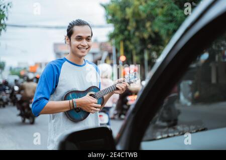 busker utilise des instruments de musique et chante devant le voiture lorsque le trafic est occupé aux feux de signalisation carrefour Banque D'Images