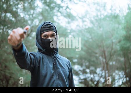 voleur dans un masque et port noir de sweat à capuche a pointé le placez le couteau à côté de l'espace de copie lorsque vous vous tenez sur le forêt Banque D'Images