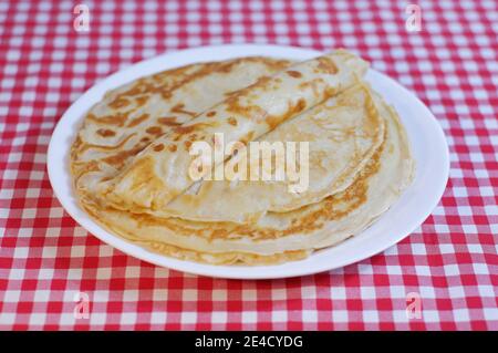 De délicieuses crêpes frites sont empilées sur une assiette sur une nappe à carreaux. Banque D'Images