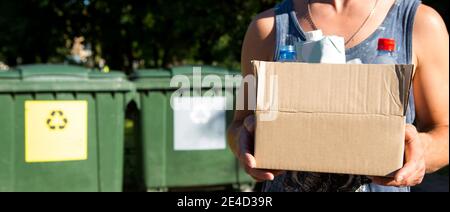 Une boîte en carton contenant des ordures dans les mains d'un homme près de conteneurs pour la collecte séparée des déchets. Conscience écologique de la population, soins pour Banque D'Images