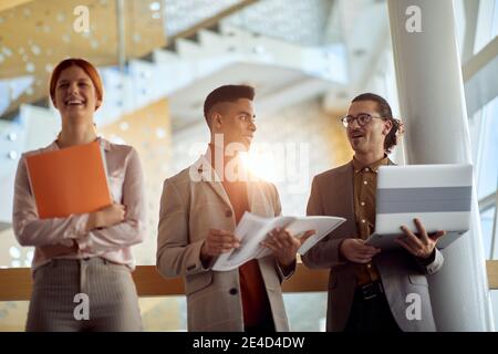 jeune femme caucasienne riant à la discussion de deux coléeagues mâles dans le couloir du bâtiment d'affaires Banque D'Images