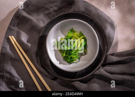 Salade japonaise aux algues wakame vertes sur deux assiettes, une serviette grise et une paire de baguettes Banque D'Images