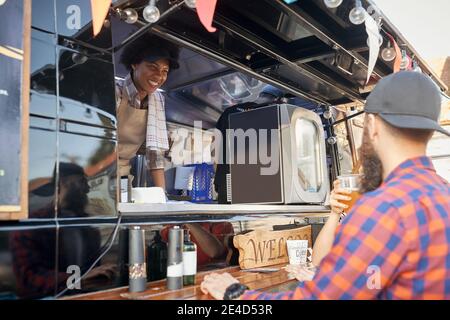 jeune femme afro-américaine dans le service de restauration rapide ayant une conversation avec les clients, souriant Banque D'Images