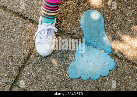 Pied de petite fille à côté du grand pied peint sur le trottoir, grand pied bleu peint sur la route,. Banque D'Images