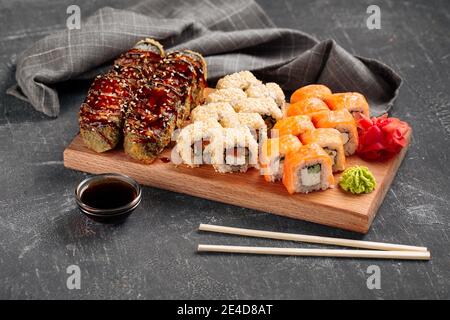 Vue latérale sur un assortiment de petits pains à sushis sur une planche de bois avec de la sauce au wasabi et au soja Banque D'Images