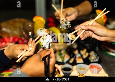 Les gens tiennent les rouleaux de sushis avec des bâtons. Couples qui mangent et partagent des sushis roulés, maki, nigiri, uramaki. Concept alimentaire. Banque D'Images