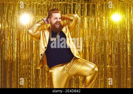 Joyeux homme à barbe confiant en costume de fête doré dansant et s'amuser au club de discothèque Banque D'Images