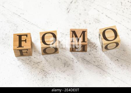 Quatre cubes en bois avec des lettres FOMO (c'est-à-dire peur de manquer) sur le tableau blanc. Banque D'Images