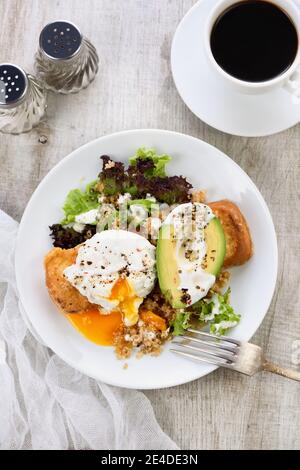 Une assiette de petit déjeuner saine et équilibrée. L'œuf de Benedict se répand sur un toast grillé avec un demi-avocat, un quinoa et une laitue, des épices assaisonnées et du yogu Banque D'Images