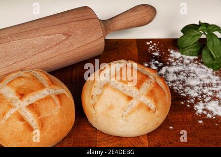 Petits pains frais sur une planche de bois saupoudrés de farine et d'une broche roulante en arrière-plan. Prise de vue en studio Banque D'Images