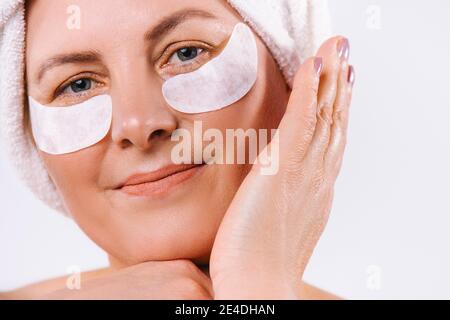 Une photo agrandie d'une femme âgée avec une serviette sur sa tête et des cellules oculaires regardant la caméra sur un fond blanc. Banque D'Images