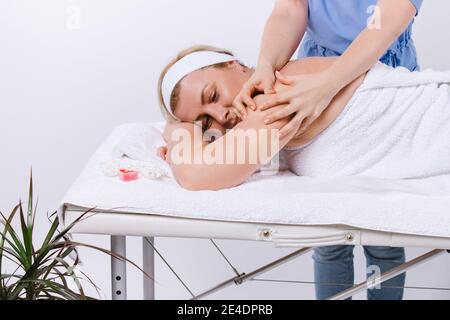 Maître masseuse fait un massage sur fond blanc à une femme dans le salon avec des bougies aromatiques. Photo rognée Banque D'Images