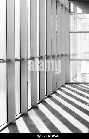 Image verticale en niveaux de gris d'un couloir intérieur avec de grandes fenêtres et des ombres sur le sol Banque D'Images