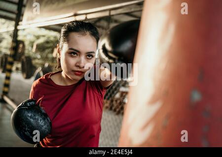 femme boxer combattant faisant l'exercice frappant sac de poinçonnage avec copyspace au camp de boxe Banque D'Images