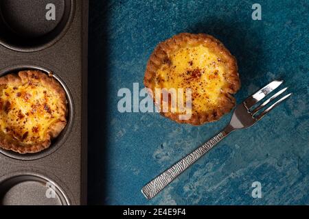 Une tarte aux œufs fraîchement cuite avec un fourche à gâteau posée sur le côté et plaque de cuisson contenant une autre tarte Banque D'Images