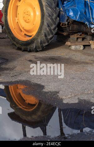 roue jaune du tracteur reflétée dans la flaque de pluie Banque D'Images