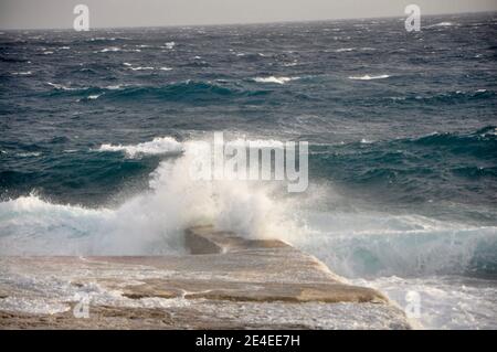 Une vague de tempête éclabousse sur la jetée en pierre sur la côte de l'île croate. Une grande vague de sarcelle éclabousse au centre de la jetée en pierre vide le jour d'hiver ensoleillé. Banque D'Images