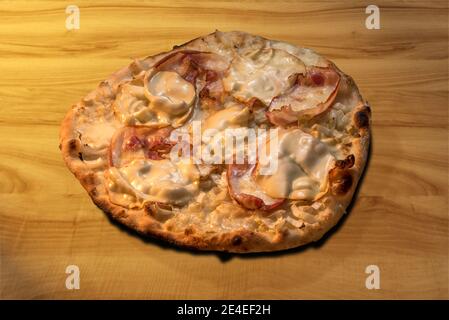 Pizza au fromage Scamorza, Pancetta au porc fumé plat et chicorée blanche. Lumière chaude sur planche à découper en bois Banque D'Images