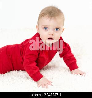 Un petit enfant se trouve sur son ventre sur un tapis blanc. Banque D'Images