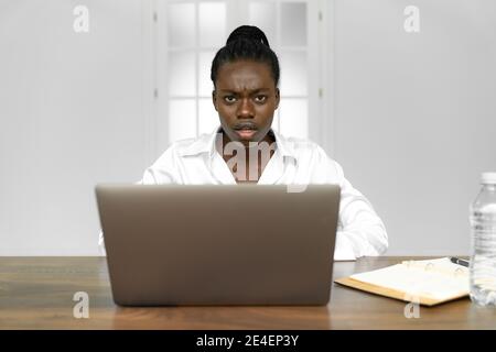 Une jeune femme confuse s'assoit au bureau à la maison, travaille à l'ordinateur portable regarder la caméra se rendre compte de l'échéance manquante, frustrée déception fille se sentent la perplexe Banque D'Images