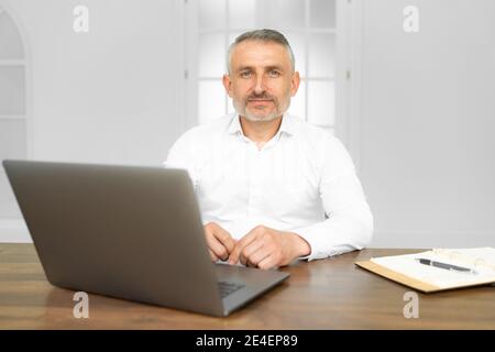Homme d'affaires en âge moyen portant une cravate assise à l'aide d'un ordinateur portable au bureau avec une expression sérieuse sur le visage. Simple et naturel regarder le est venu Banque D'Images