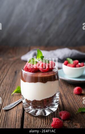 Délicieux dessert en couches avec fromage à la crème, biscuits au chocolat écrasé, nappés de ganache et de framboises fraîches dans un pot Banque D'Images