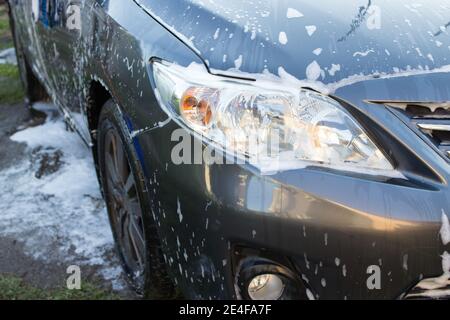 Concept de lavage de voiture, voiture sombre en mousse. Phare d'un gros plan de voiture noir Banque D'Images