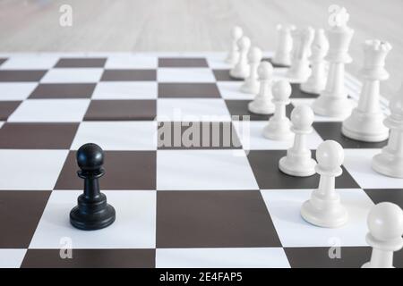 Pion noir solitaire devant une armée blanche de pièces d'échecs Banque D'Images