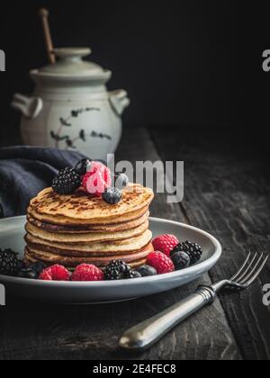 Crêpes aux baies fraîches - bleuets, framboises et mûres sur plaque et table en bois vintage. Pot de miel sur fond flou. Banque D'Images