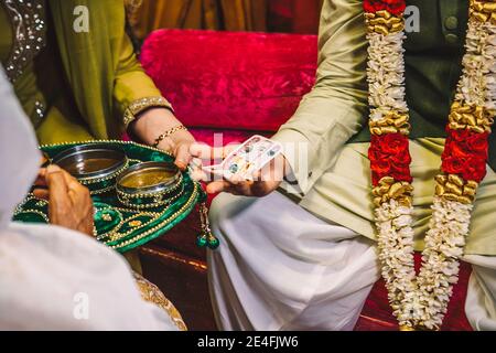 Mains des expatriés indiens pakistanais à Dubaï, Émirats arabes Unis pendant les rituels de la nuit de mariage sangeet, femmes et marié avec de l'argent dirhams dans les mains, mehndi assiette en velours Banque D'Images