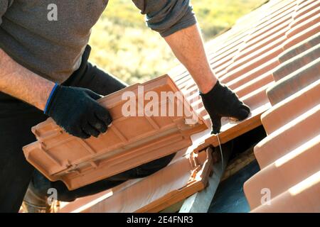 Gros plan des mains du travailleur installant des tuiles de toiture en céramique jaune montées sur des panneaux en bois recouvrant le toit d'un bâtiment résidentiel en construction. Banque D'Images