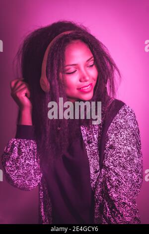 Portrait rose fluo clair d'une belle femme hispanique souriante écouter de la musique sur un casque Banque D'Images