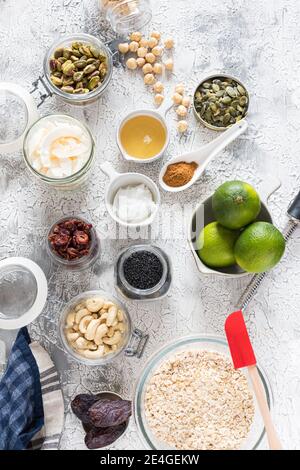 Vue en hauteur de quelques ingrédients de granola crus dans des pots en verre et des bols sur un fond gris et blanc rustique. Banque D'Images