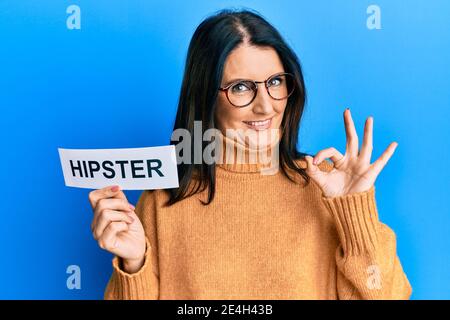 Moyenne âge brune femme tenant le papier avec hipster mot faisant signe ok avec les doigts, souriant sympathique gestante excellent symbole Banque D'Images