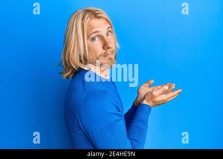 Un jeune homme caucasien aux cheveux longs se présentant avec des paumes ouvertes, tenant quelque chose d'expression sans indice et confuse. Doute concept. Banque D'Images