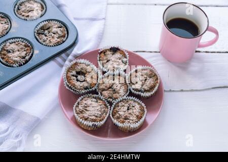 Des muffins aux flocons d'avoine sains sur une assiette rose et une tasse de café sur une table en bois blanc, vue du dessus. Banque D'Images