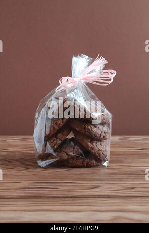 Biscuits d'avoine au chocolat dans un sac transparent sur une table en bois contre un mur brun. Gros plan Banque D'Images