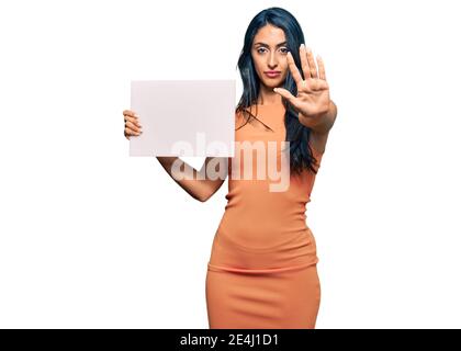 Belle femme hispanique tenant vide bannière avec main ouverte faisant signe d'arrêt avec l'expression sérieuse et confiante, geste de défense Banque D'Images