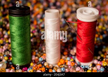 Fils vert, blanc et rouge ensemble. La bobine rouge a une aiguille à l'intérieur et les trois objets sont au-dessus de perles de plusieurs couleurs Banque D'Images