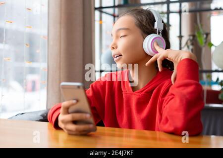 Une adolescente écoute de la musique via un casque et chante - application en ligne sur un téléphone portable. Concept de technologie moderne. Banque D'Images