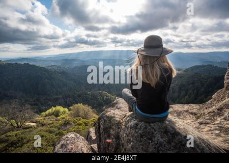 Une femme s'assoit au-dessus des collines boisées et de la nature sauvage des montagnes de Santa Cruz en Californie. Banque D'Images